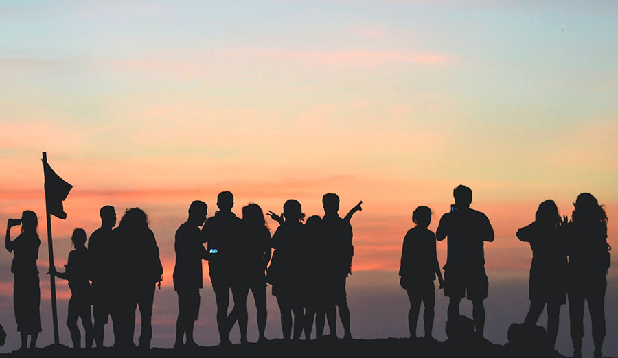 Silhouettes of people standing in front of a sunset